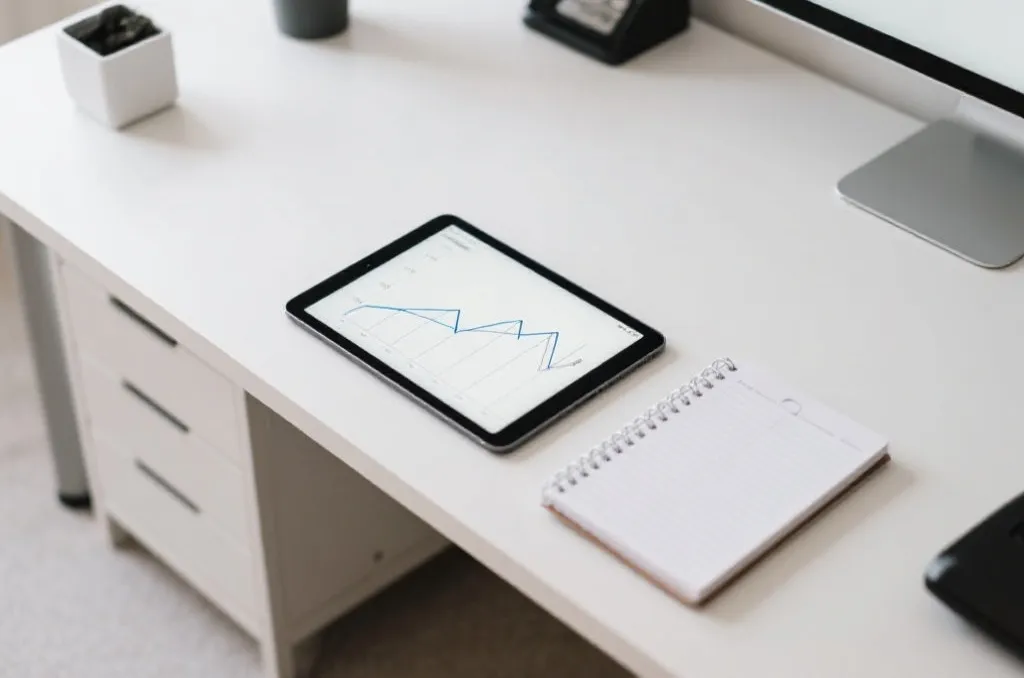 An overhead view of a minimalist office desk with a tablet showing clean line graphs and a neat planner notebook